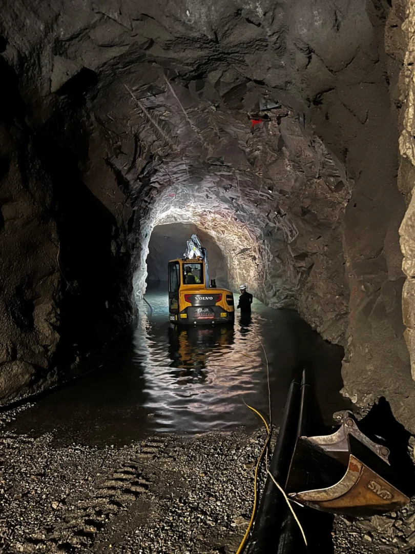 Flooded rock tunnel lit by work lights, with cable laid along its floor