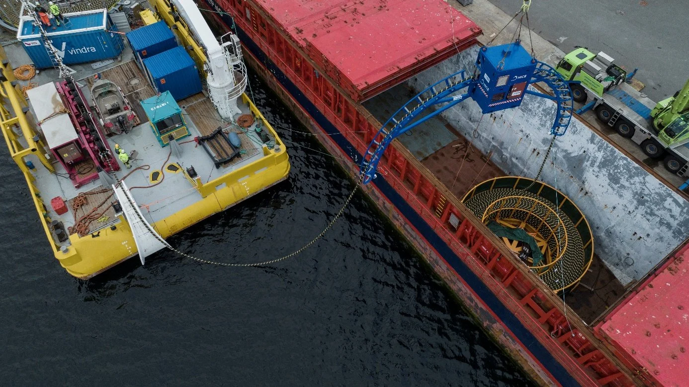Cable barge and transport vessel moored side by side, seen from above, with cable running between them