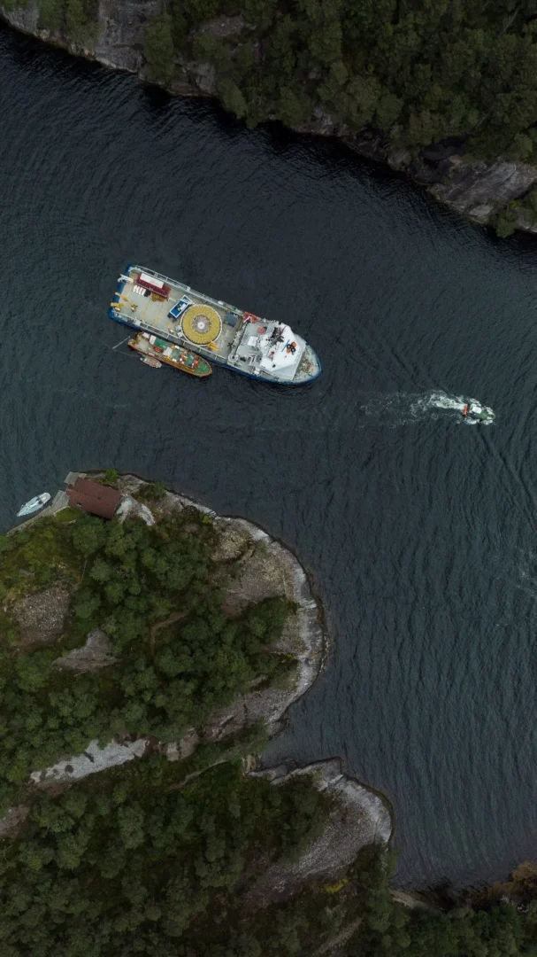 Cable-laying vessel and workboat in a narrow fjord passage, seen from directly above